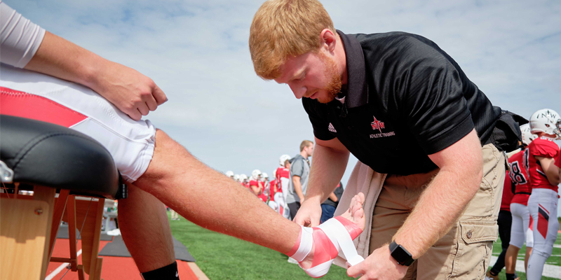 Athletic training student taping a football player's ankel