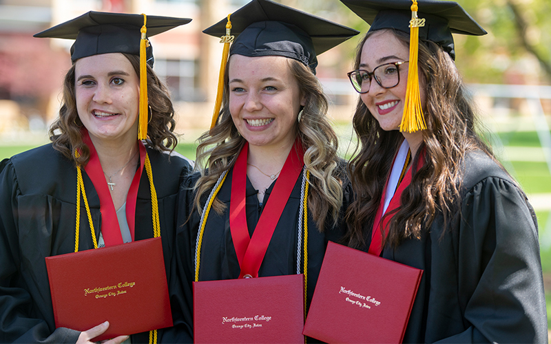 Three graduates pose for a photograph with diplomas