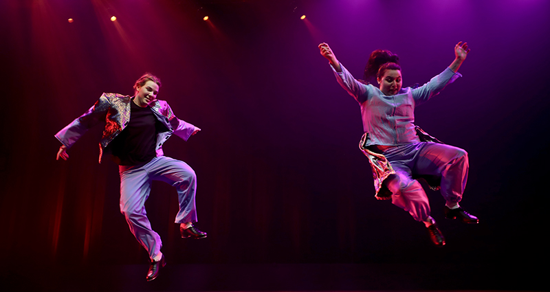 Two dancers leap in the air during a performance of RUSH