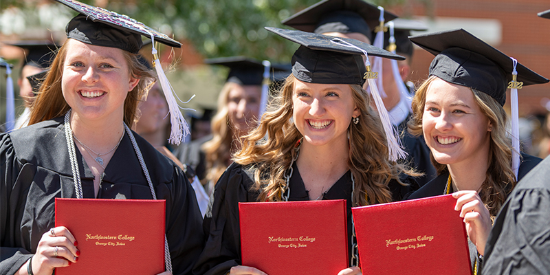 Three graduates proudly display their diplomas