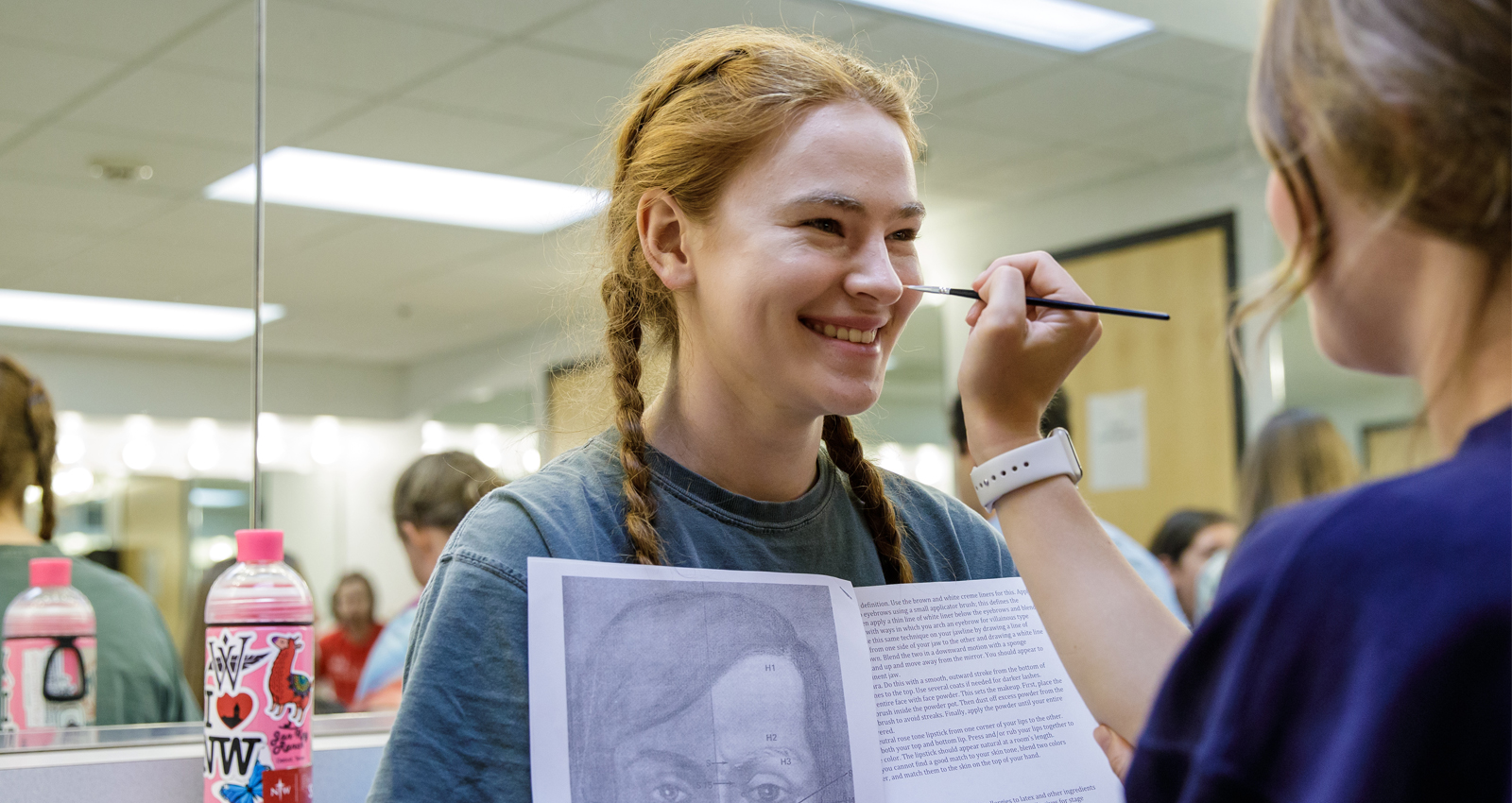 A high school student applies stage makeup to another student